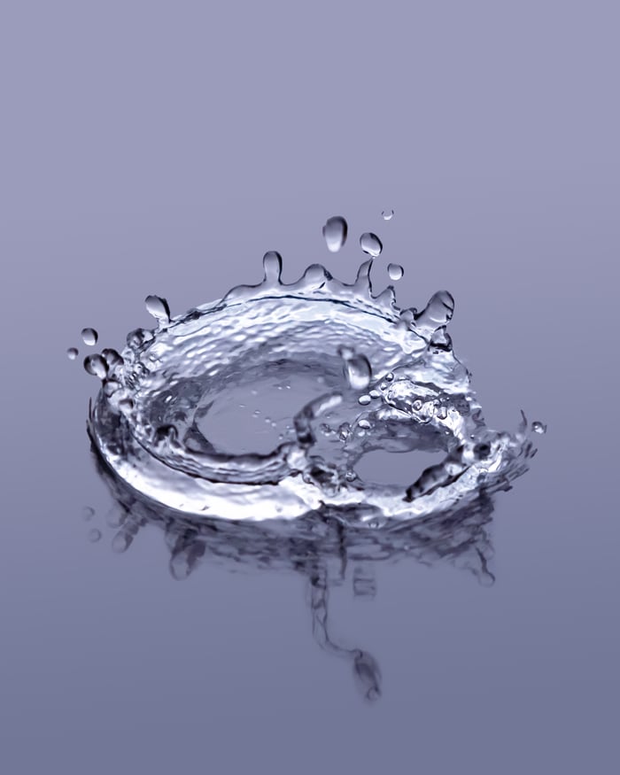 Dynamic close-up of a water drop splash with intricate reflection on a gray background.